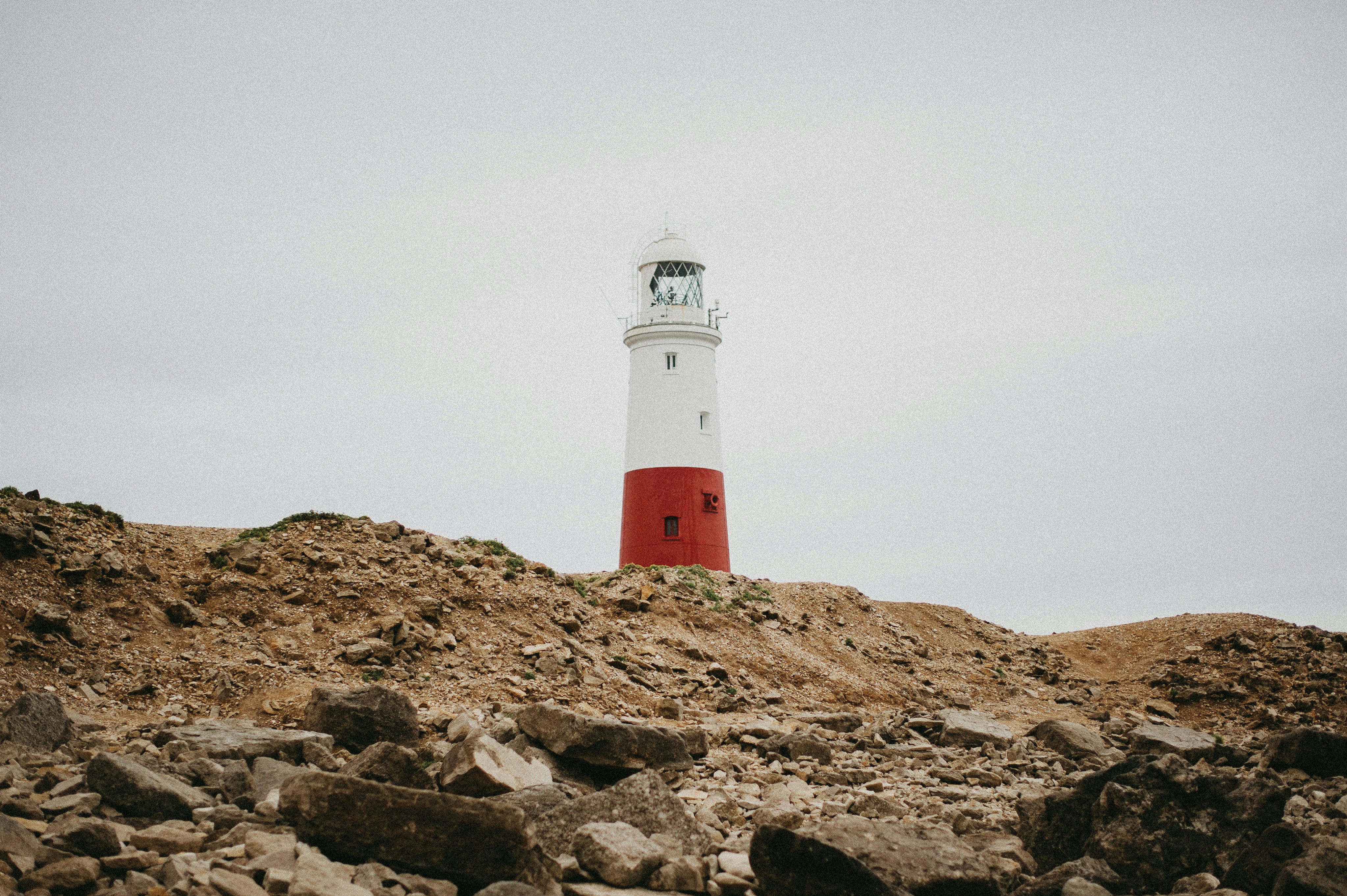 red and white lighthouse on brown rocky mountain under white sky during daytime